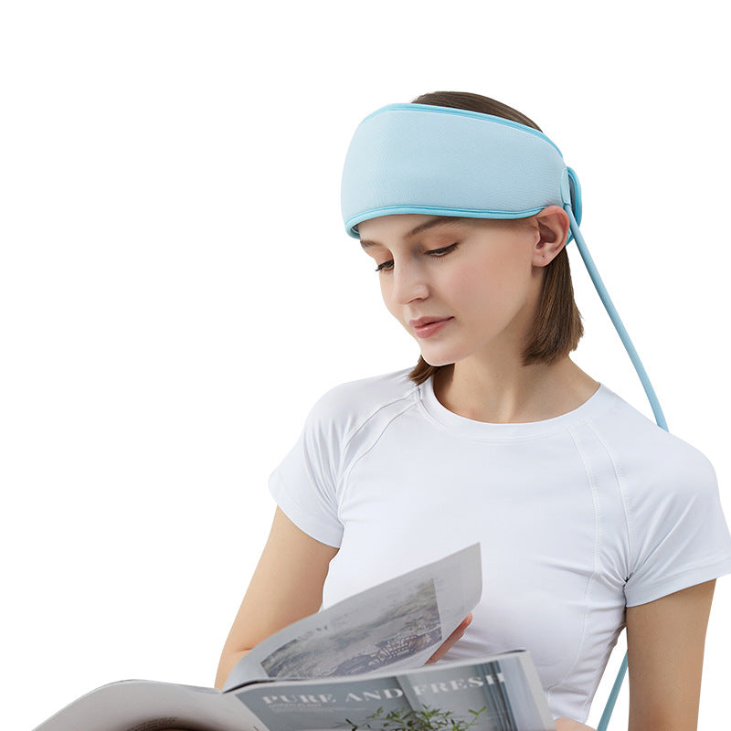 Person wearing a light blue sleep mask while reading a magazine on a white background